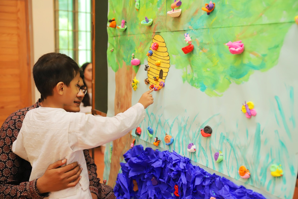 The Little Art, Lahore — a child engages with a hand-painted tree mural with clay creatures